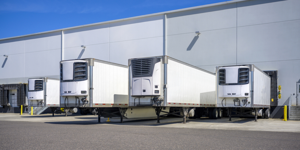 Refrigerator semi trailers without semi trucks standing at warehouse dock gates loading frozen cargo for next freight