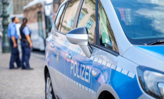 German police car stands on street. Two police officers controls traffic. Polizei is the german word for police